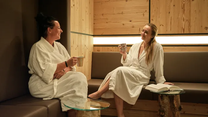 Zwei Frauen in Bademänteln entspannen mit Tee in einer Holz-Wellnesslounge